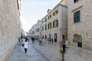 Uma rua de pedra com edifícios históricos, alguns com lojas e outros com janelas em arco.
