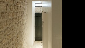 A hallway with a stone wall, wooden ceiling beams, and a white door at the end. - Apartments Eleganca (Dubrovnik)