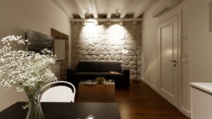 A cozy living room with a stone wall, a dark sofa, a wooden coffee table, and a vase of flowers. - Apartments Eleganca (Dubrovnik)