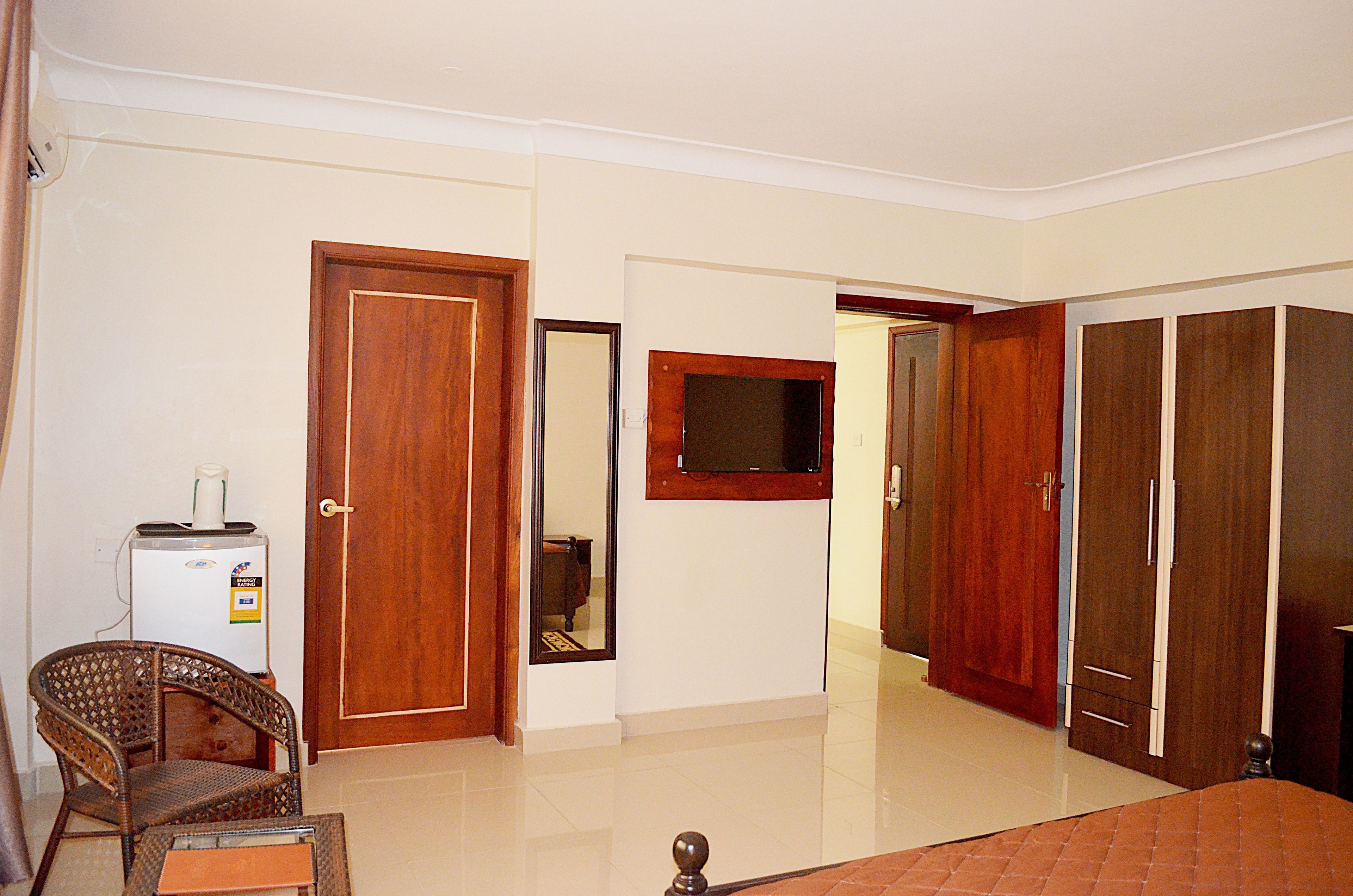 A hotel room with a bed, a wooden wardrobe, a television mounted on the wall, a small table, and a chair.
