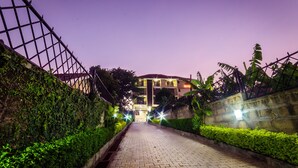 A paved pathway leading to a building with a red roof, surrounded by greenery and illuminated by streetlights. - Marie's Royale Hotel (Kampala)