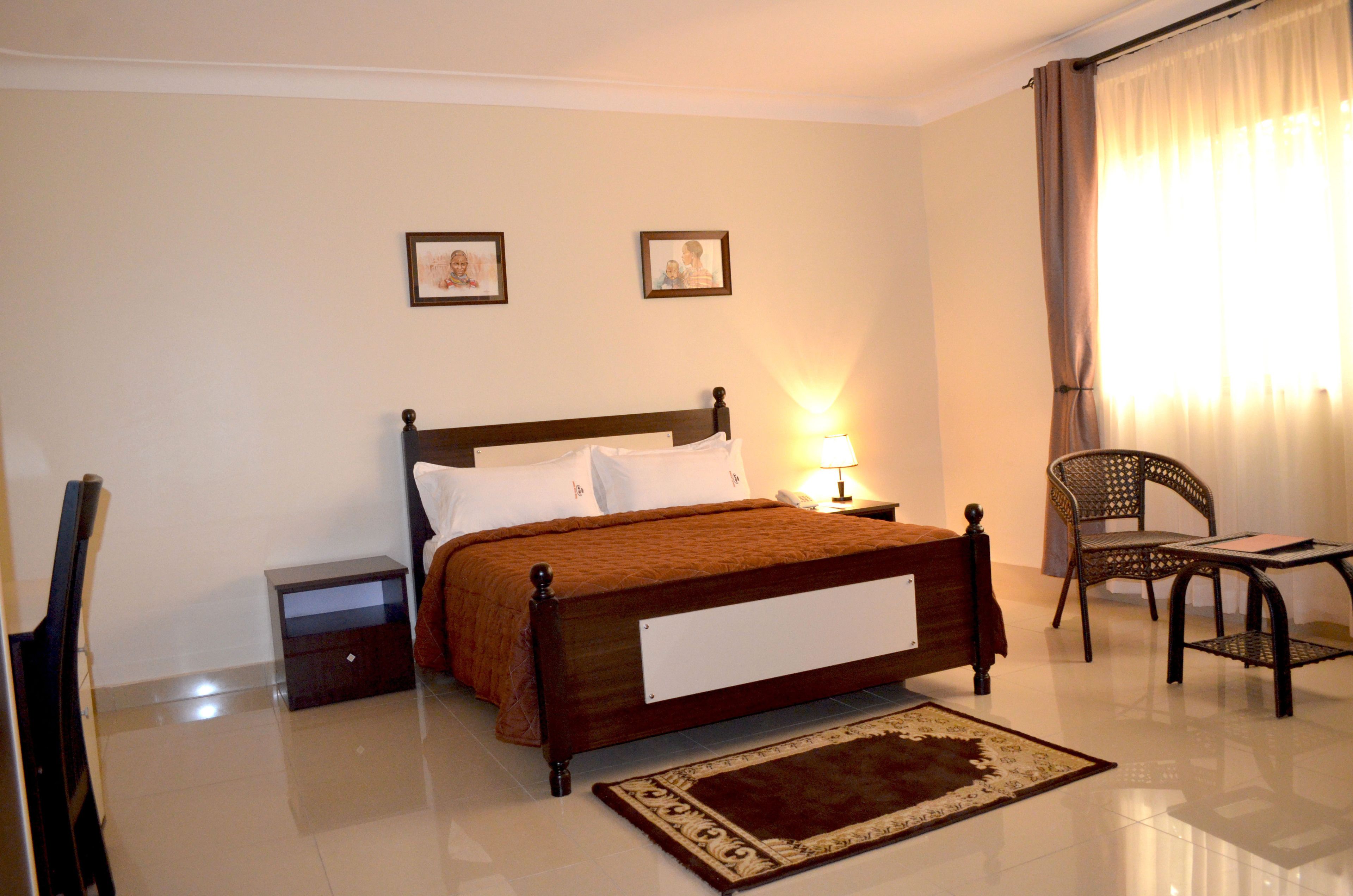 A neatly arranged bedroom with a wooden bed, a bedside table, a chair, and two framed pictures on the wall.