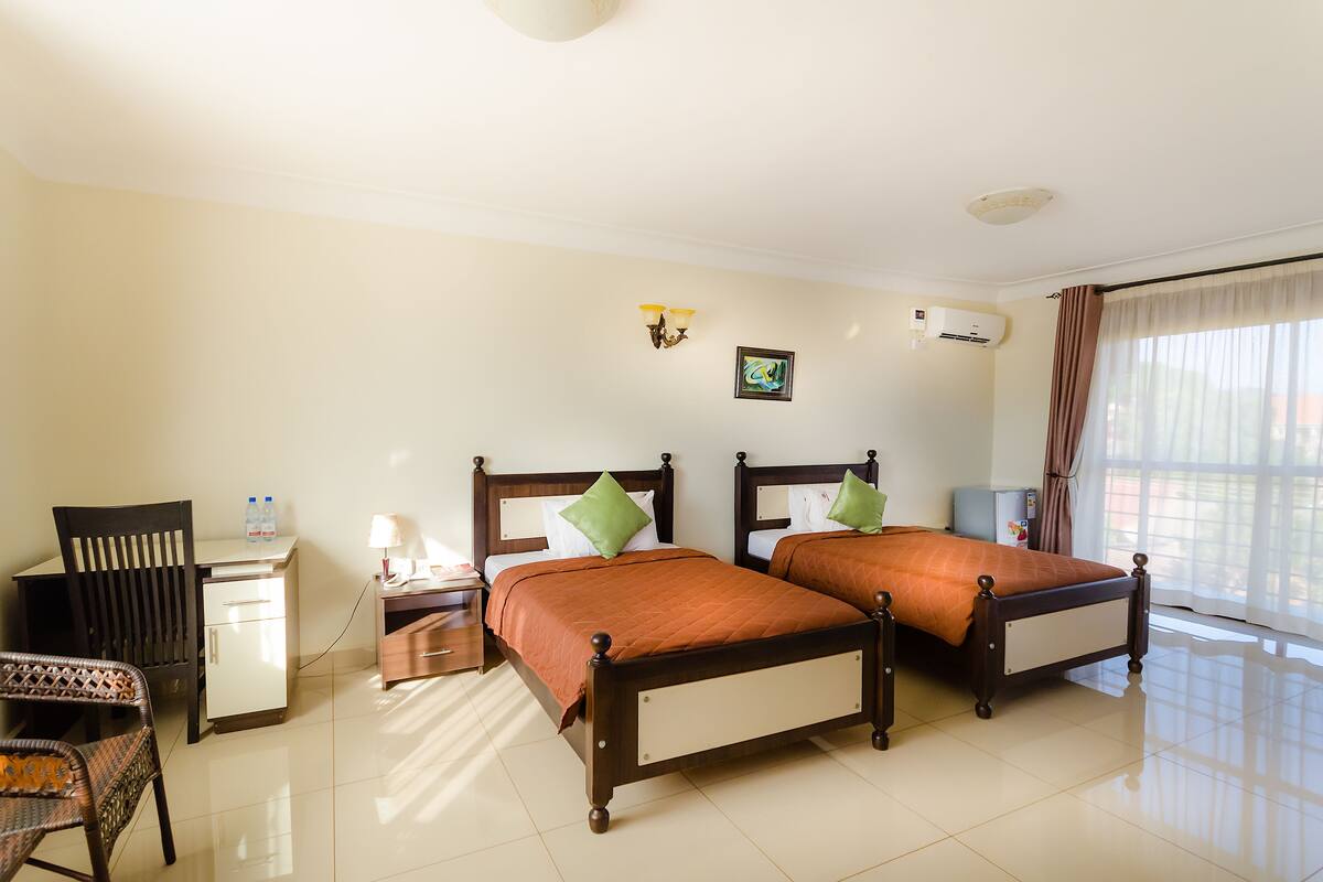 A hotel room with two beds, a desk, a chair, a nightstand, and a window with curtains.