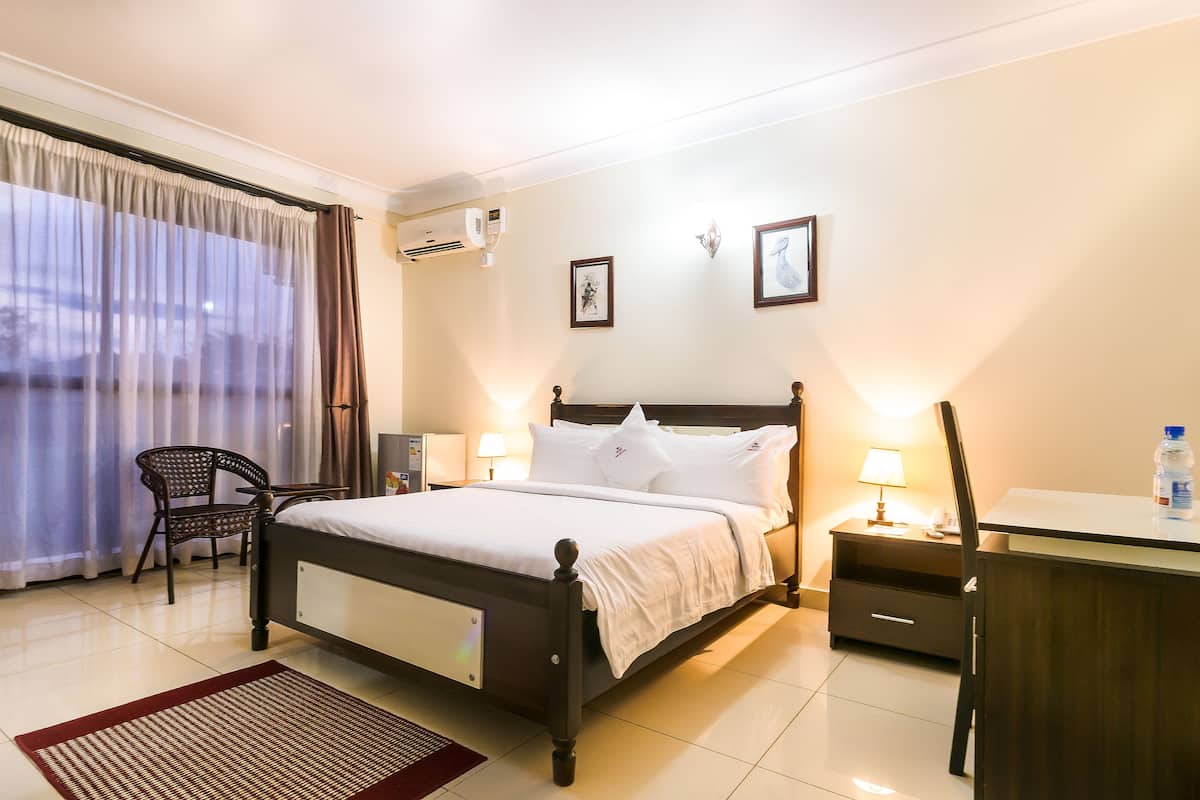 A hotel room with a bed, bedside tables, a desk, a chair, and a window with curtains.