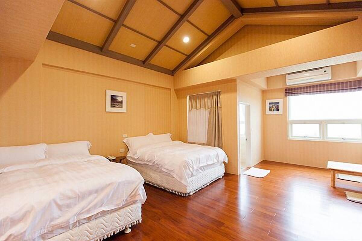 Habitació d'hotel amb dos llits, terres de fusta, una finestra gran amb cortines i un aparell d'aire condicionat.