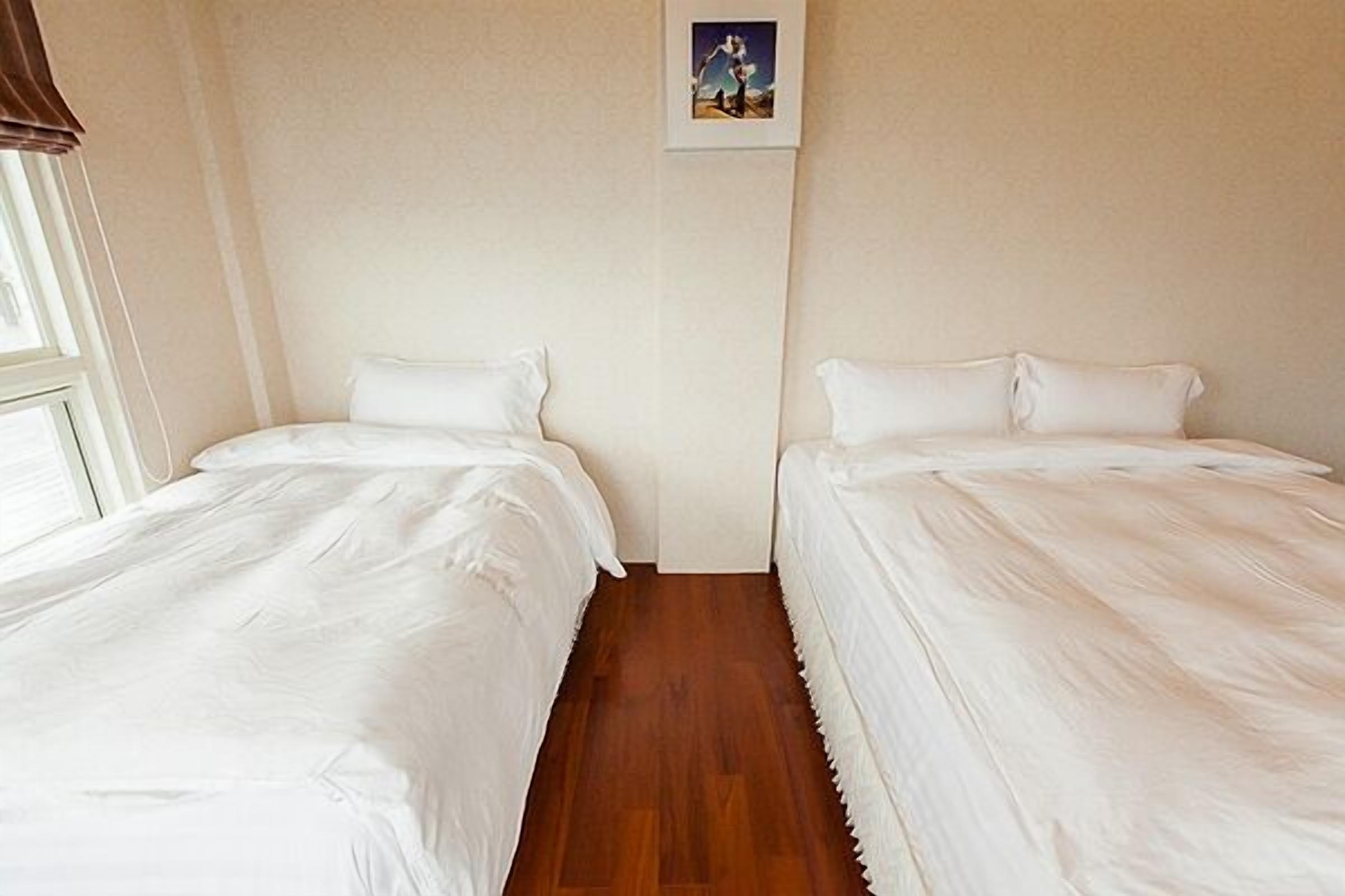 A room with two single beds, wooden flooring, and a framed picture on the wall.