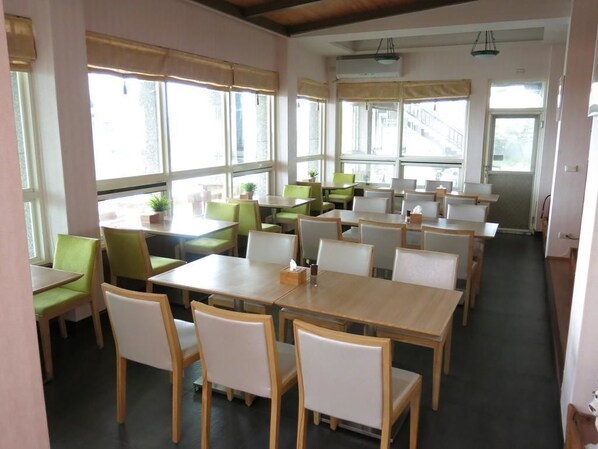 A dining area with multiple tables and chairs, large windows, and a ceiling fan. - Fully One B and B (Taitung)