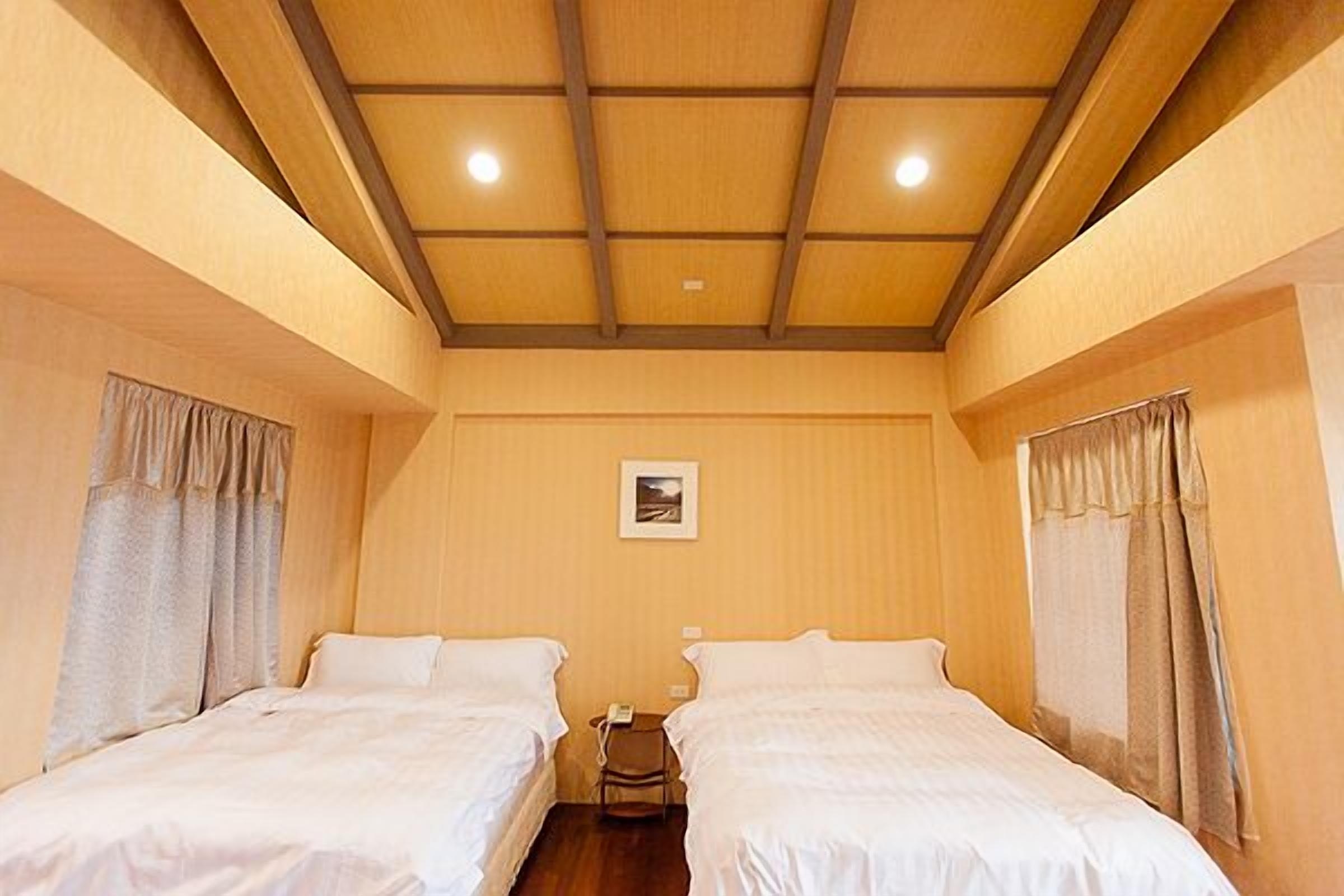 A hotel room with two single beds, a wooden ceiling, and a small table with a phone.