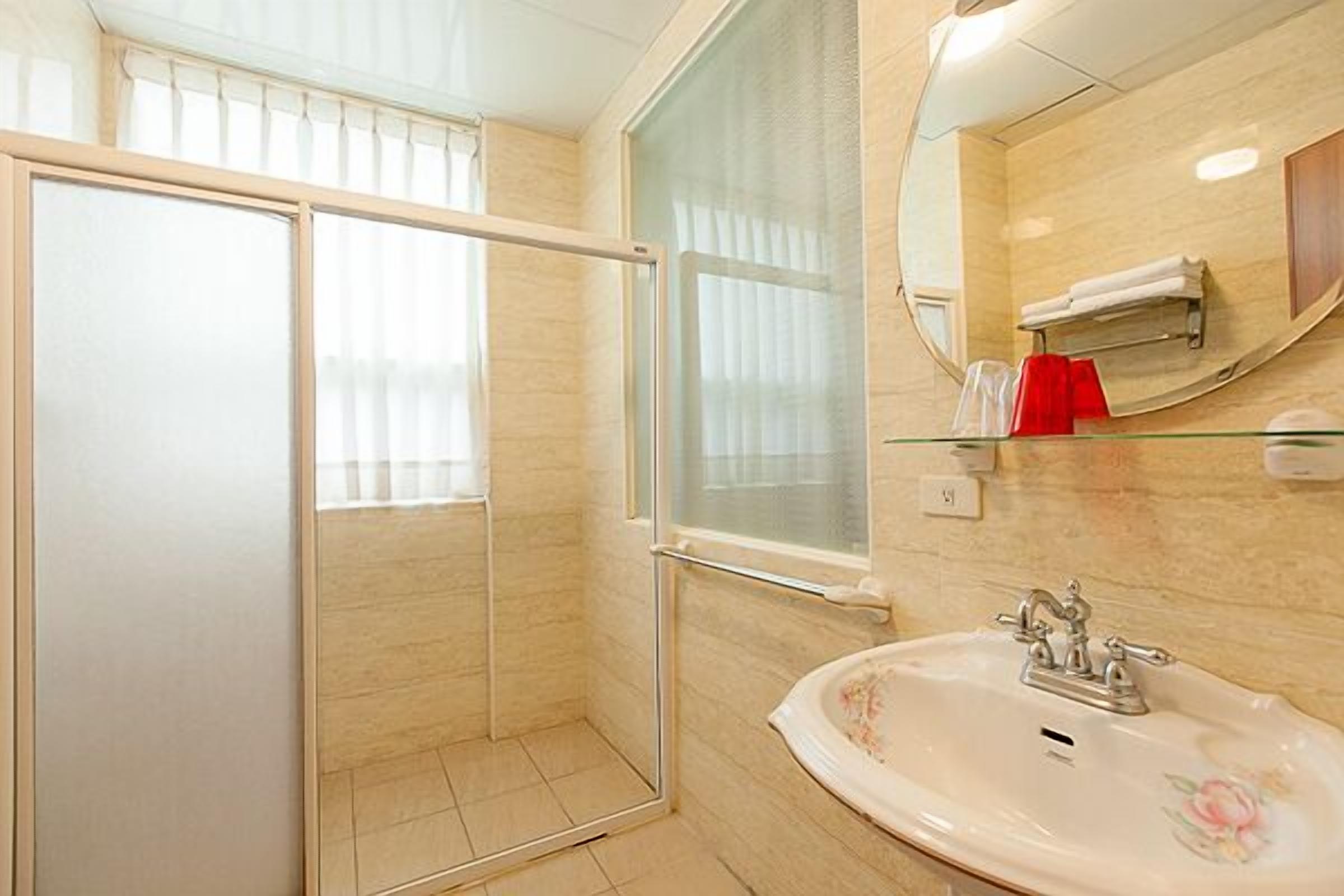 A bathroom with a glass shower enclosure, a sink with floral design, and a mirror with a towel rack.