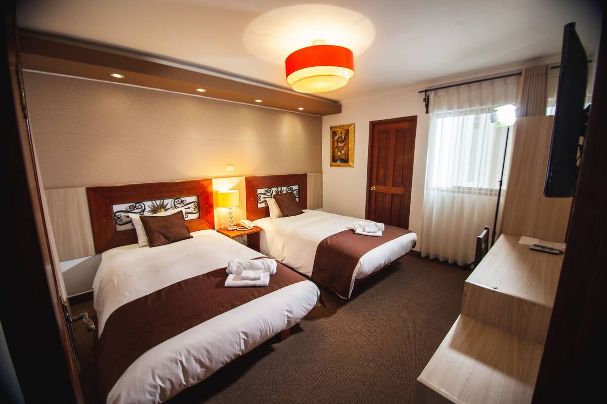 A hotel room with two beds, a desk, a television, and a bathroom door.