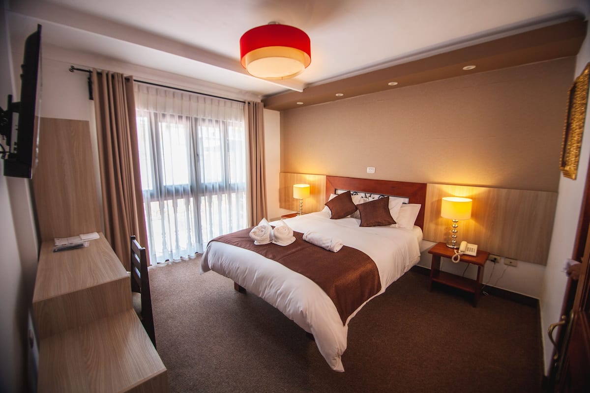 A hotel room with a large bed, two bedside lamps, a wooden nightstand, a desk, and a chair.