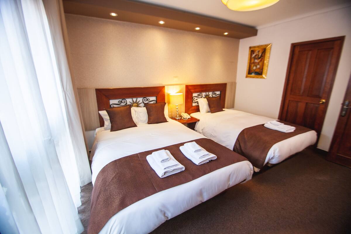 A hotel room with two beds, each with a brown headboard, white linens, and a brown blanket. There is a painting on the wall and a wooden door.