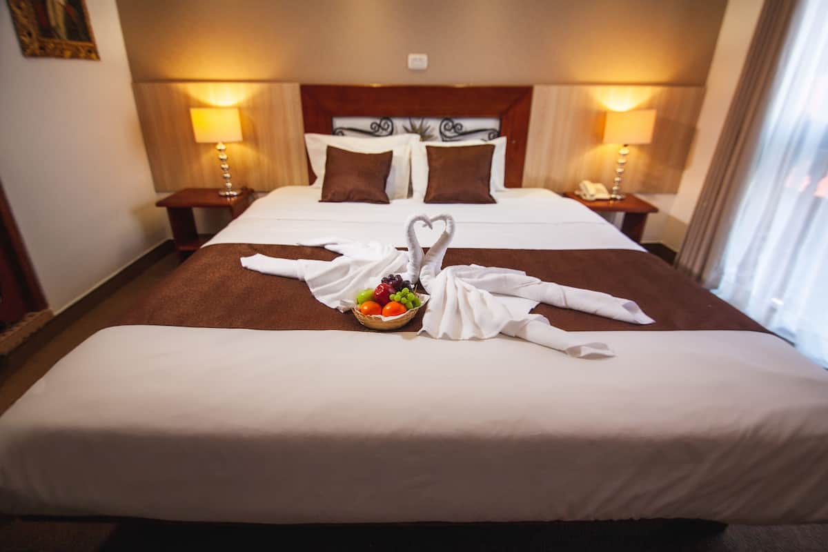A hotel room with a neatly made bed, a fruit basket, and towels arranged in a swan shape.