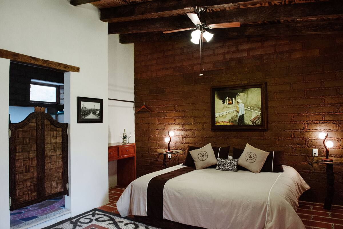 Een slaapkamer met een bakstenen muur, een bed met een wit en bruin sprei, een plafondventilator en een lijst met een afbeelding erop.