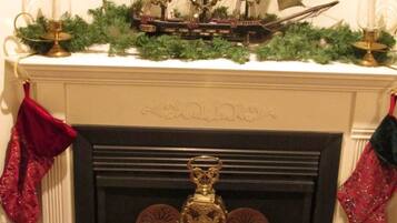 A fireplace with a ship model, framed family photos, and Christmas stockings.