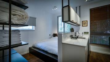Une chambre d’hôtel moderne équipée d’un lit superposé, d’une petite kitchenette et d’une fenêtre avec des stores.