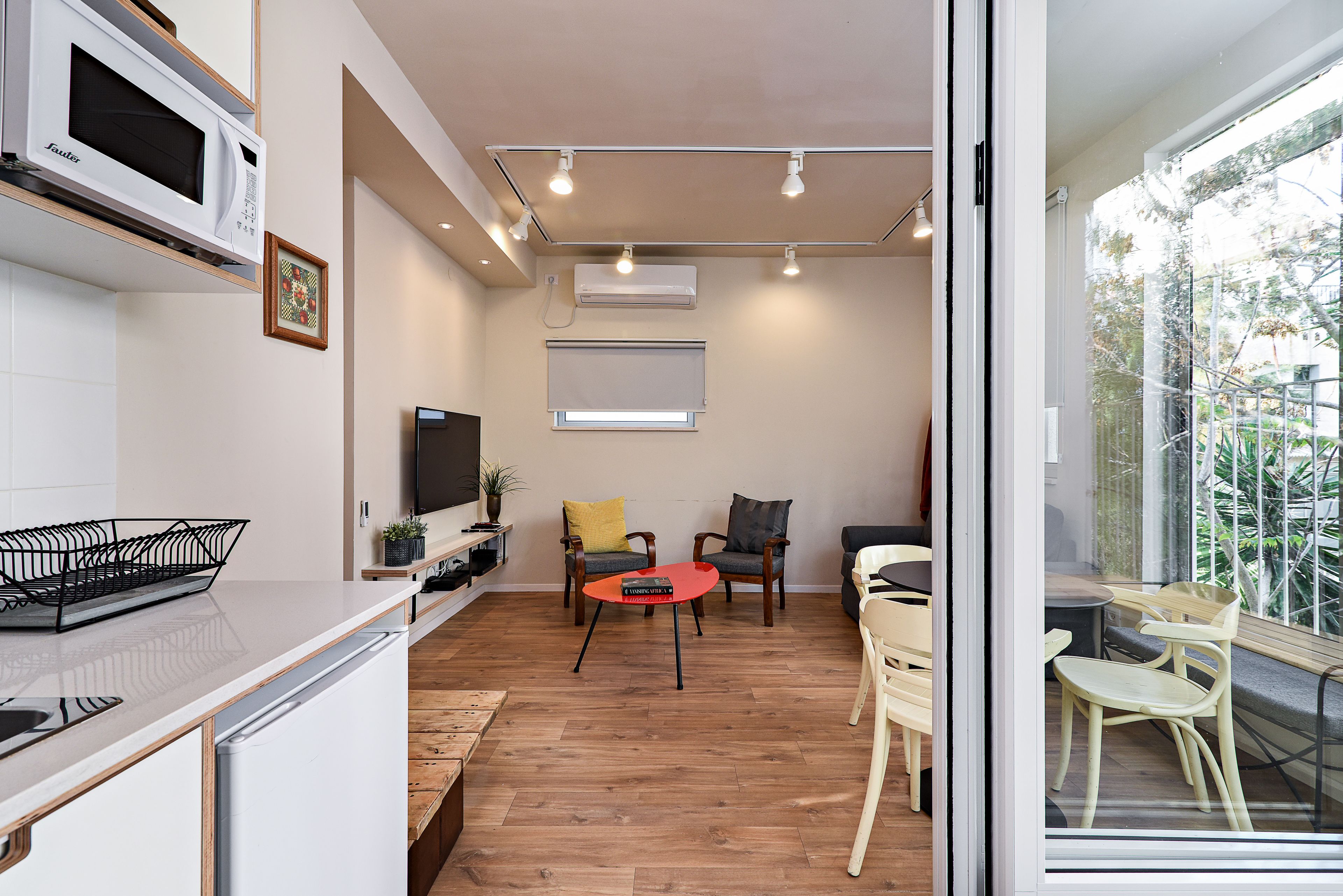 A modern kitchen with a microwave, a dining area with a red table, and a seating area with chairs.
