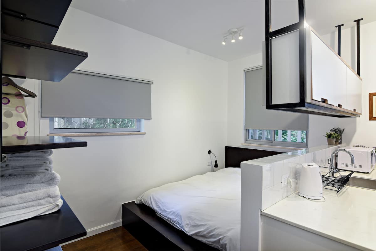 Une chambre moderne comprenant un lit, un bureau intégré, une fenêtre et un coin cuisine avec une bouilloire.