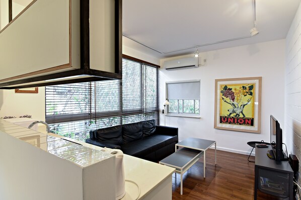 A modern kitchen with a built-in oven, a black leather sofa, a small dining table, and a framed poster on the wall. - Hanasi 129 - Boutique Apartments (Haifa)