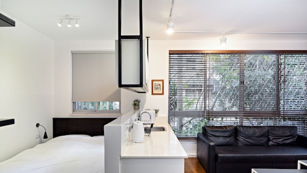 A modern, compact living space with a kitchenette, a bed, a sofa, and large windows with blinds. - Hanasi 129 - Boutique Apartments (Haifa)