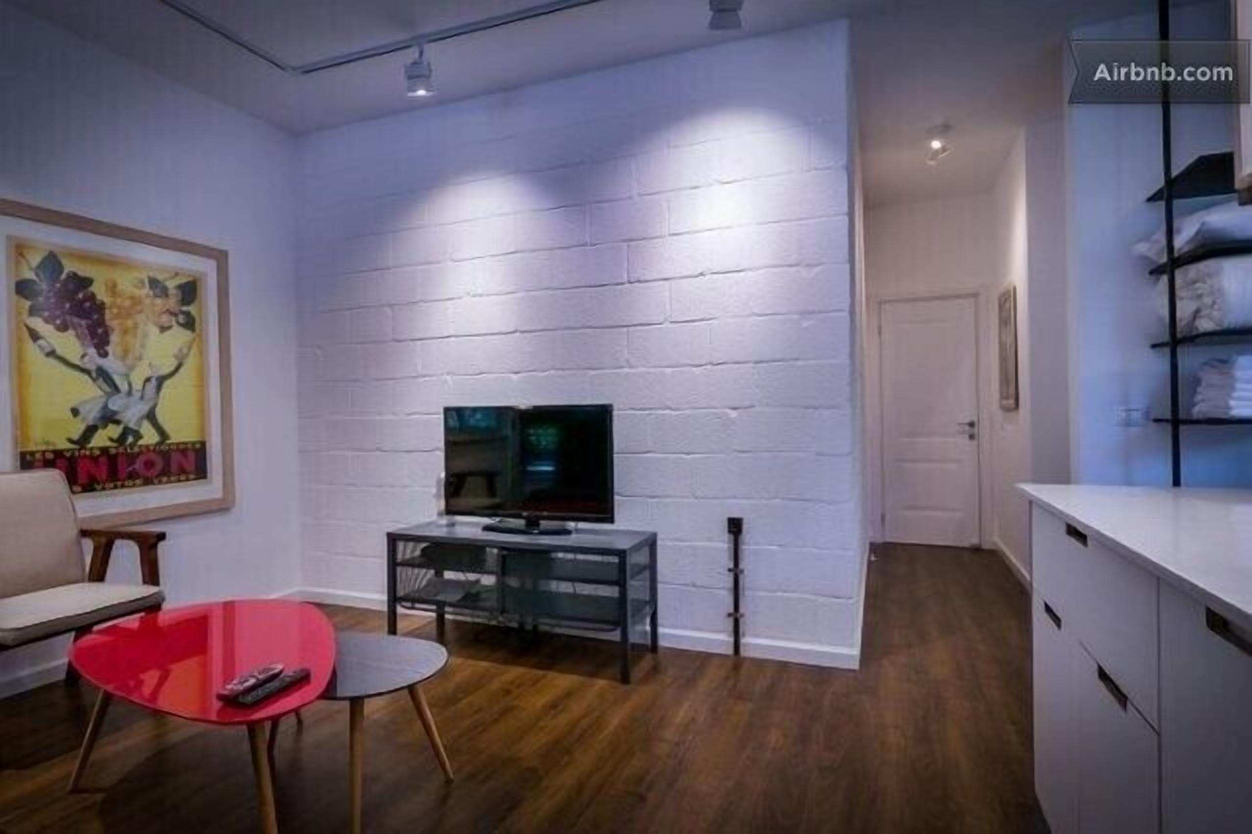 A modern living room with a flat-screen TV on a glass table, a sofa, and a red chair.