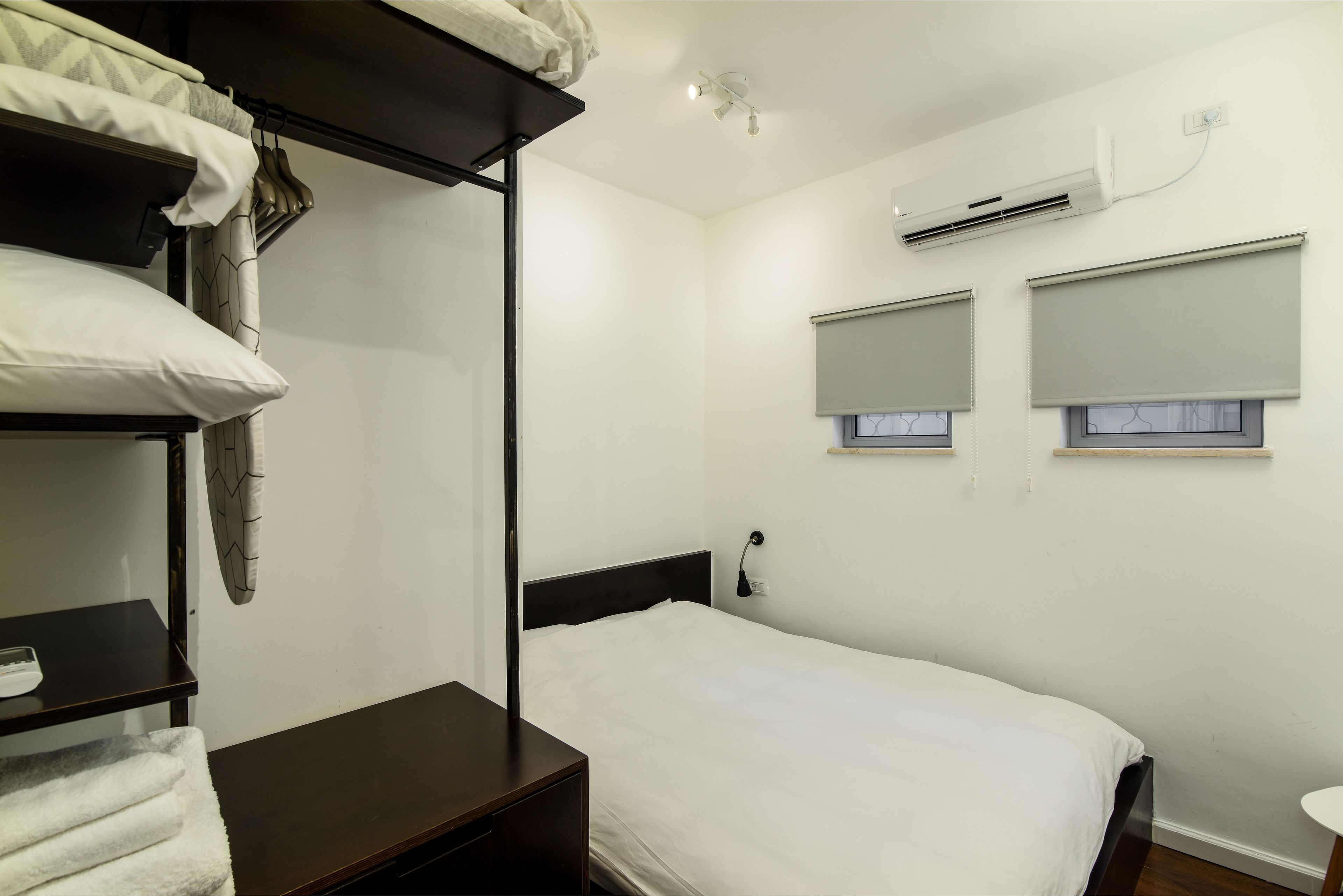 A single bed with a white mattress and dark headboard, a bedside table with a lamp, and a wall-mounted air conditioner.