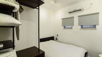 A single bed with a white mattress and dark headboard, a bedside table with a lamp, and a wall-mounted air conditioner.
