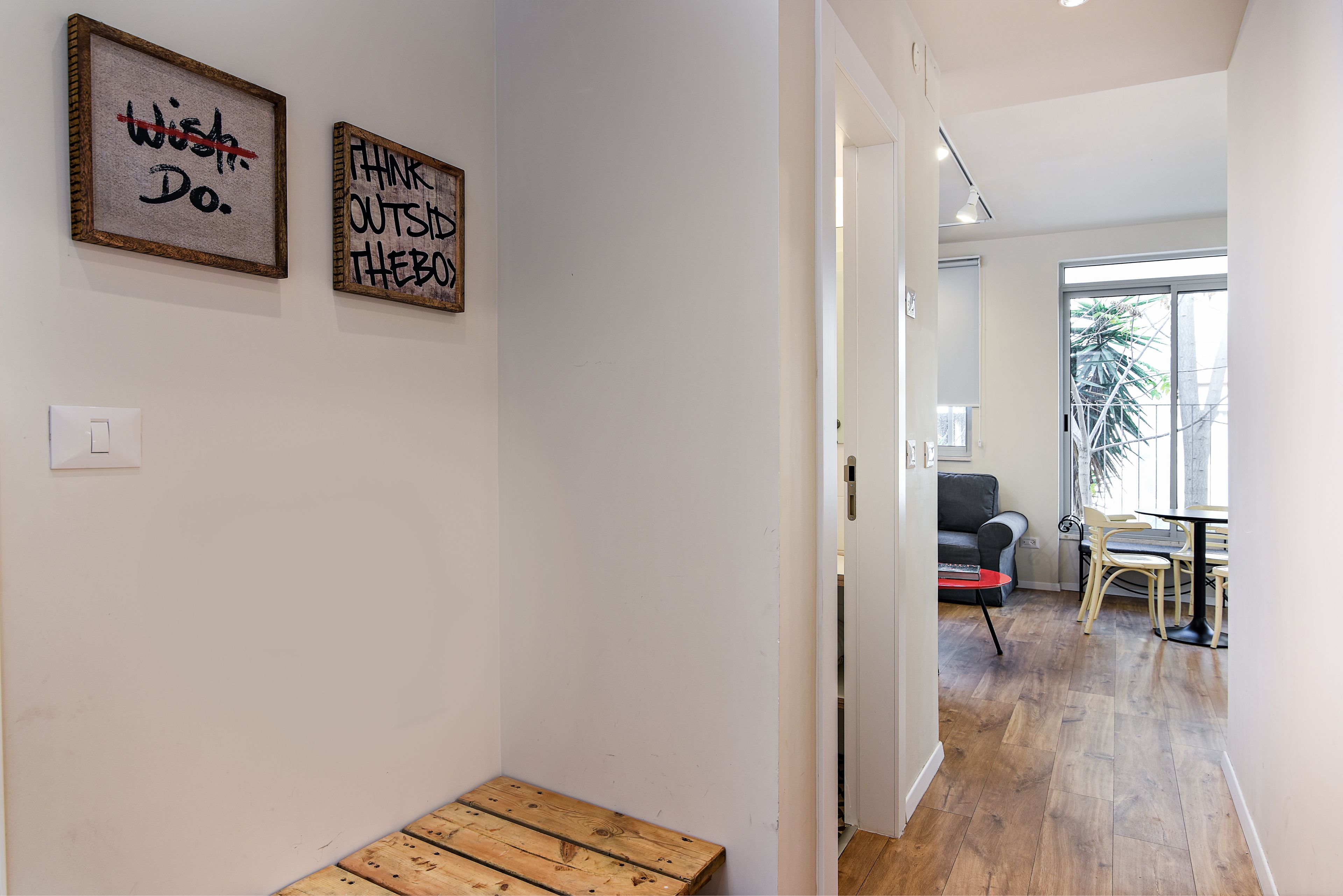 A hallway with two framed motivational posters, a wooden bench, and a view into a living area with a sofa and a dining table.