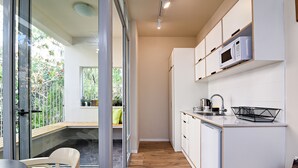 A modern kitchen with white cabinets, a microwave, and a sink. There is a wooden floor and a glass door leading to an outdoor area. - Hanasi 129 - Boutique Apartments (Haifa)