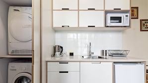 A compact kitchen with a washing machine, microwave, sink, and a small refrigerator. - Hanasi 129 - Boutique Apartments (Haifa)