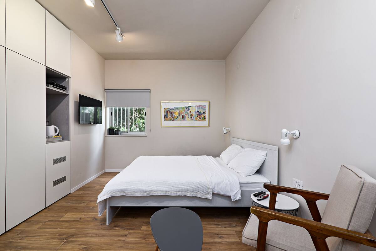 Une chambre à coucher moderne, avec un lit, une chaise, une petite table et un téléviseur fixé au mur.