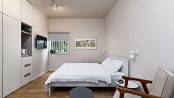 A modern bedroom with a bed, a chair, a small table, and a TV mounted on the wall.