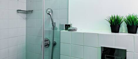 A modern bathroom with a glass shower enclosure, white tiles, and a small shelf with potted plants.