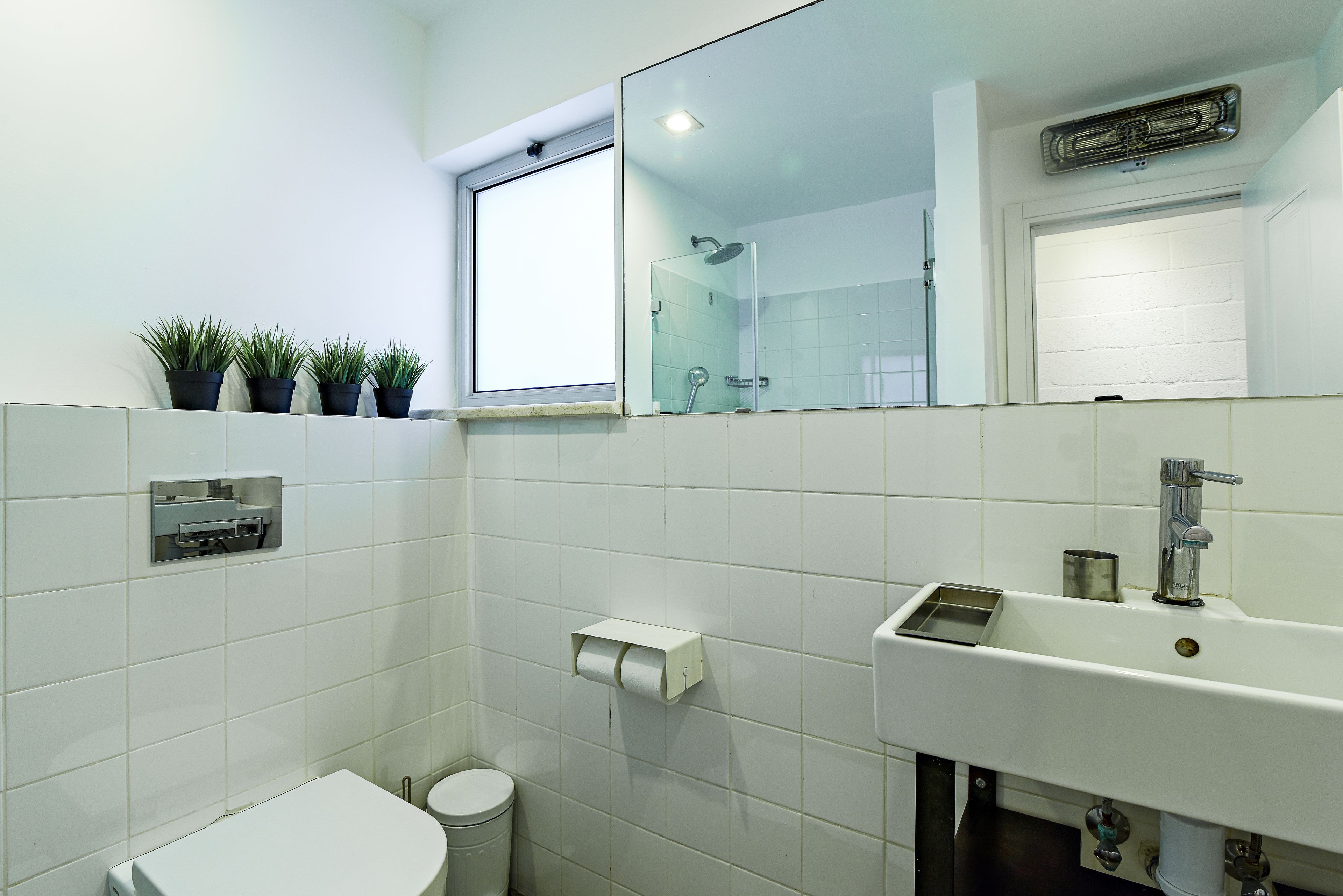 Baño con inodoro, lavamanos y ventana con plantas.