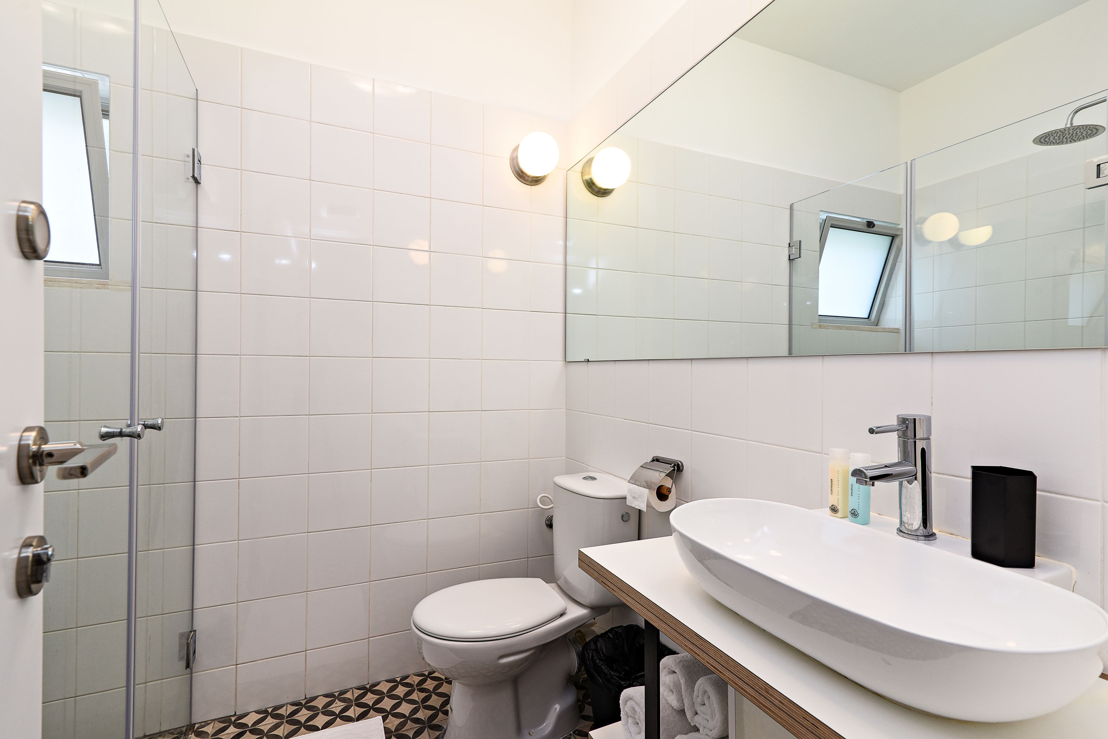 Une salle de bain moderne avec une douche à parois de verre, des toilettes blanches et un grand lavabo surmonté d’un miroir.