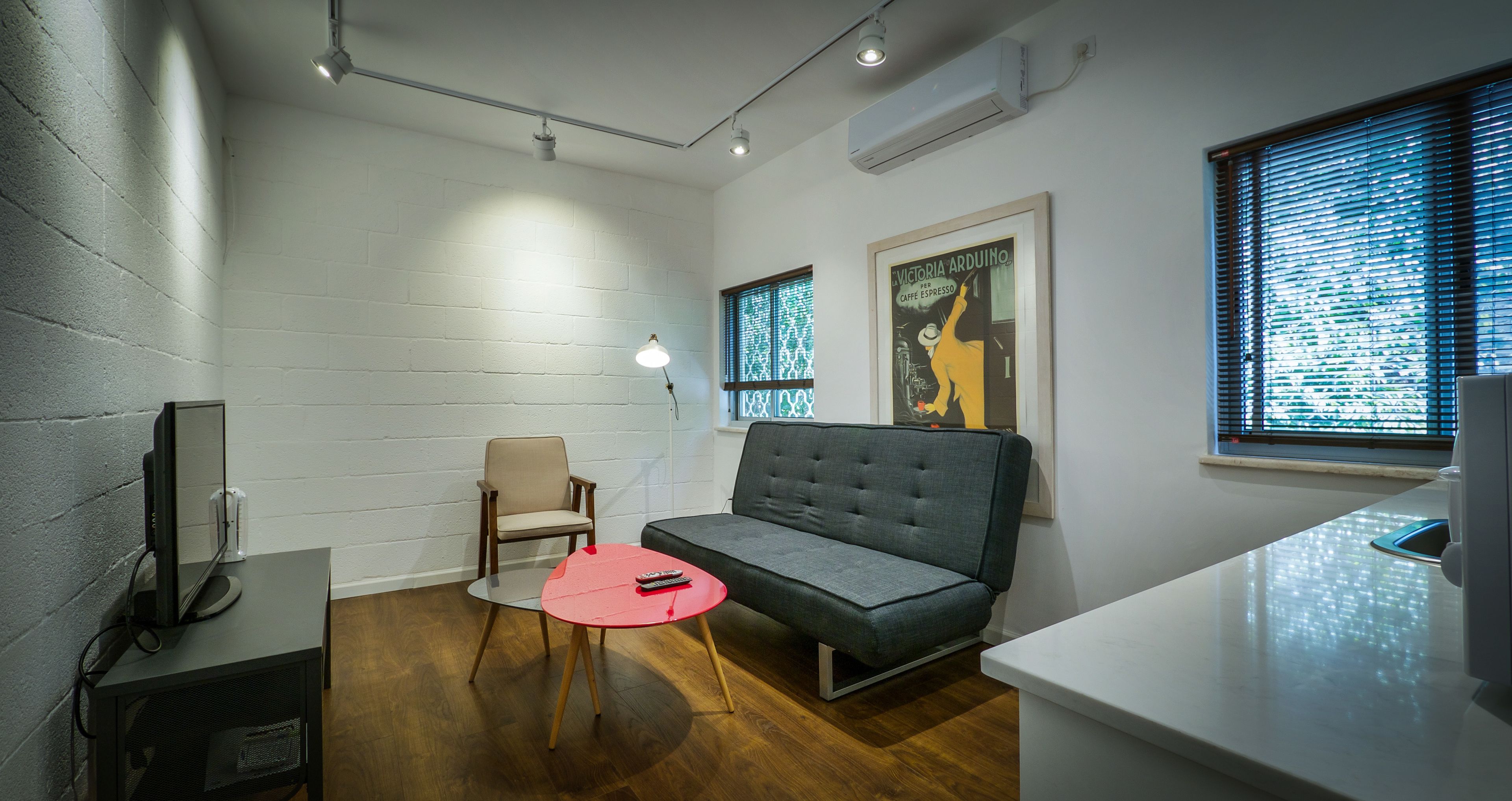 Una sala moderna con un sofá gris, una mesa roja, una silla beige y un televisor sobre un mueble.