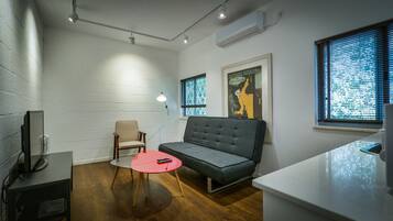 Una sala moderna con un sofá gris, una mesa roja, una silla beige y un televisor sobre un mueble.