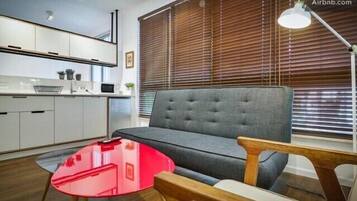 Un salon moderne avec un canapé gris, une table basse en verre rouge et des tables d’appoint en bois.