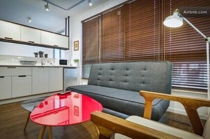 Una sala de estar moderna con un sofá gris, una mesa de centro de vidrio rojo y mesitas de noche de madera.