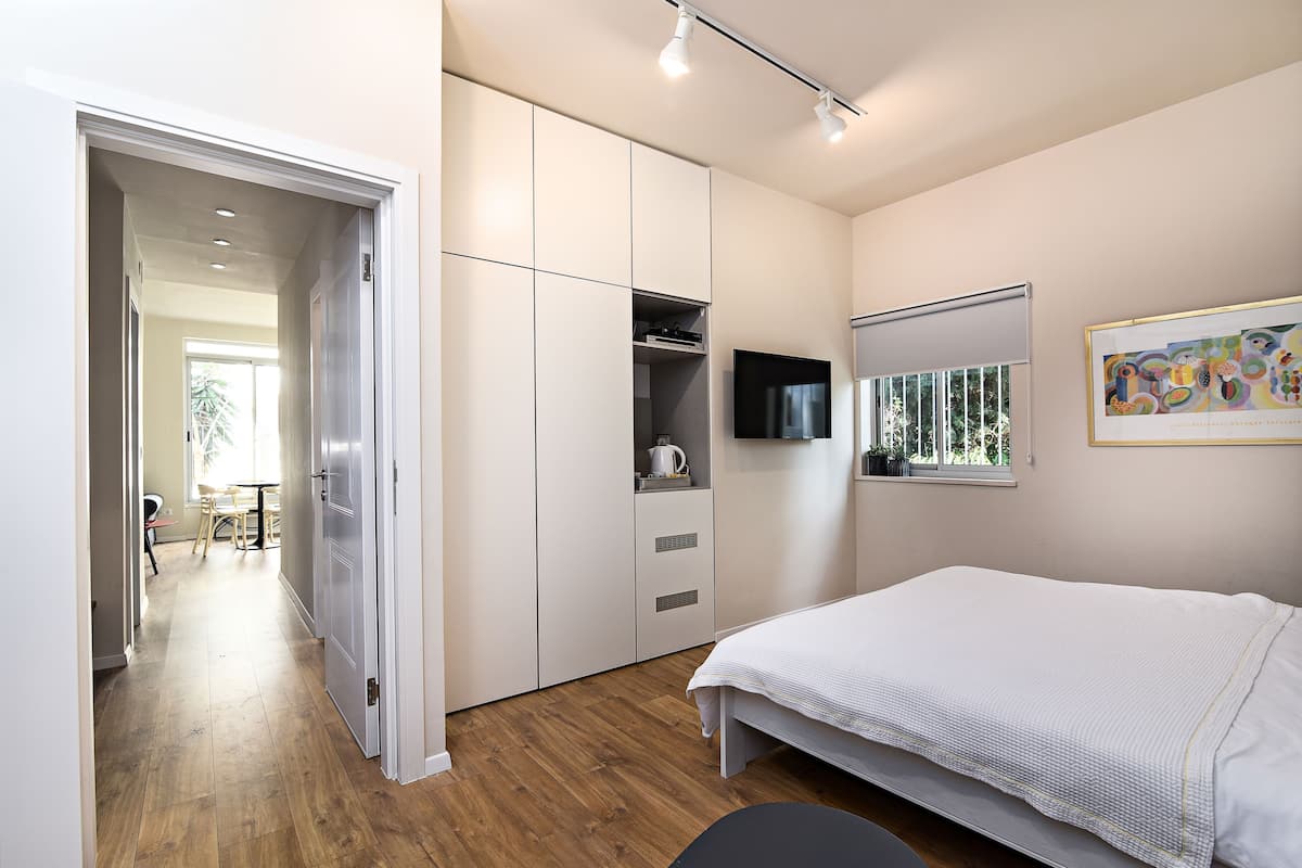 Une chambre avec un lit, une télévision, une fenêtre et une porte donnant sur un couloir.