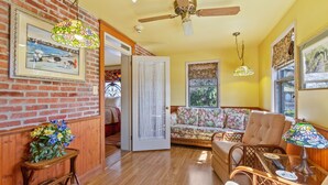 A cozy living room with a brick wall, wooden floor, a ceiling fan, a sofa, a chair, and a table with a lamp. - After Eight Bed and Breakfast (Gordonville)