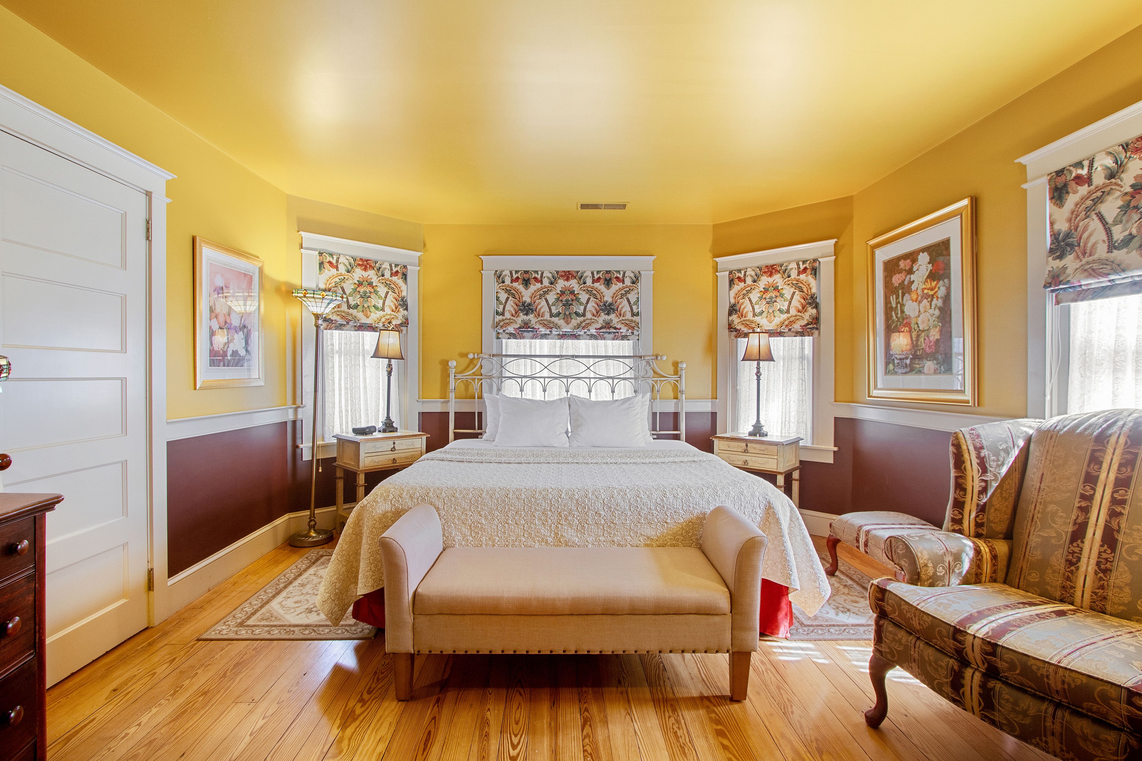 A bedroom with a large bed, a bench, two chairs, and a dresser.