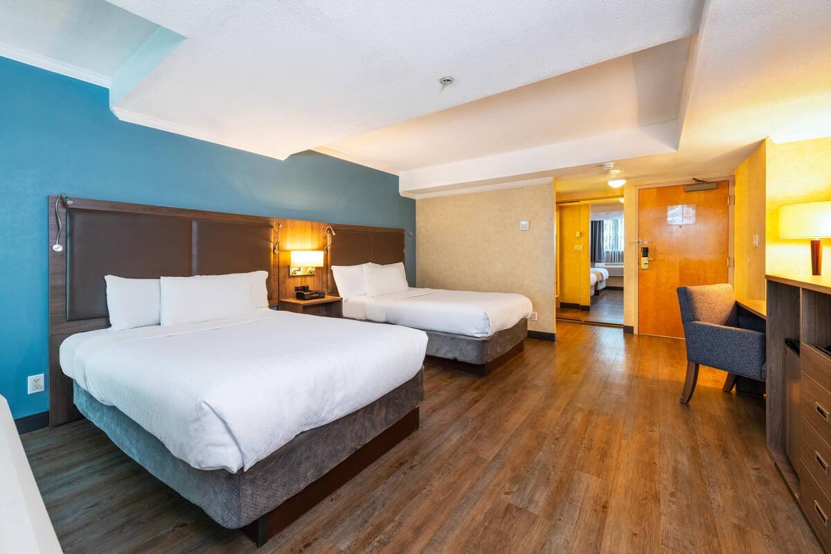 Une chambre d’hôtel avec deux lits, un bureau, une chaise et une salle de bain visible au fond.