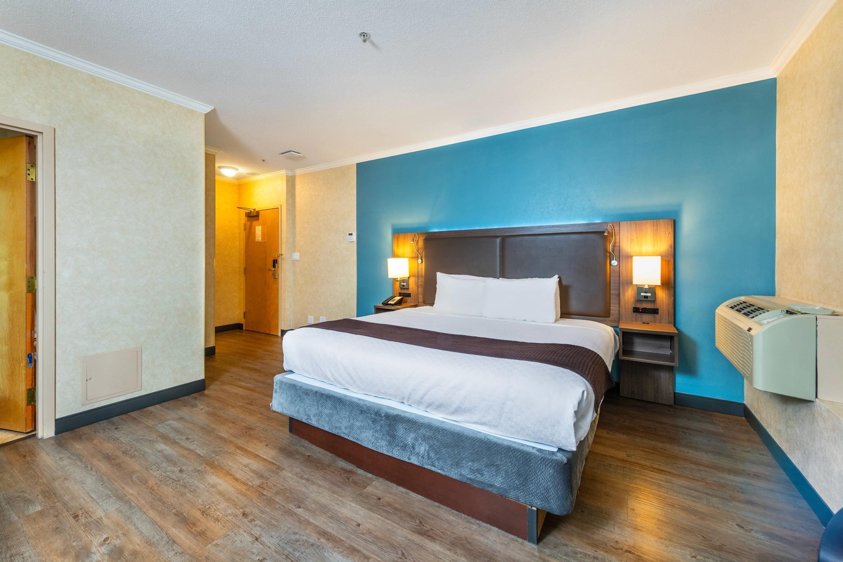 A hotel room with a large bed, two bedside lamps, a heater, and a wooden floor.