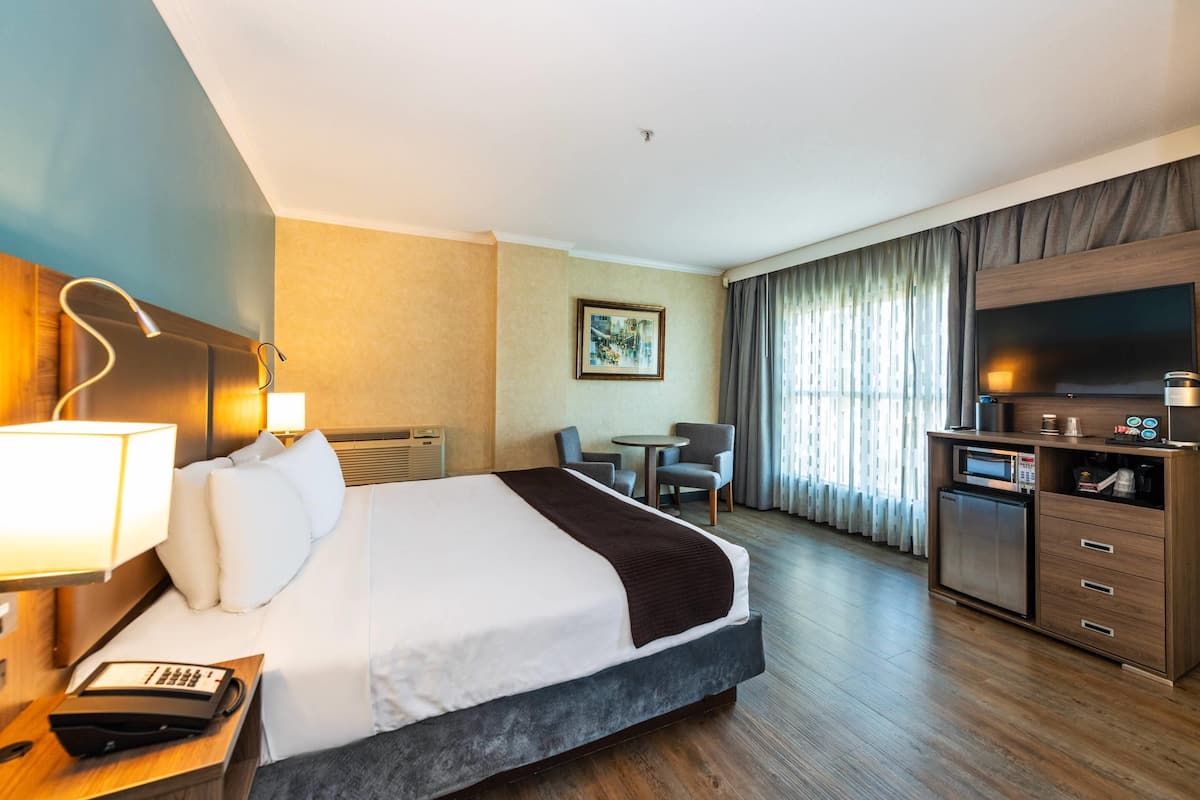Une chambre d’hôtel avec un grand lit, un bureau avec une lampe, une télévision, une petite table et un four à micro-ondes.