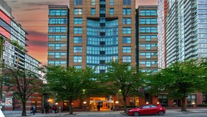 A multi-story hotel with a central entrance, surrounded by trees and other buildings.
