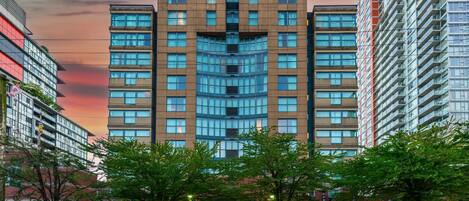 Un hotel de varios pisos con una entrada central, rodeado de árboles y otros edificios.