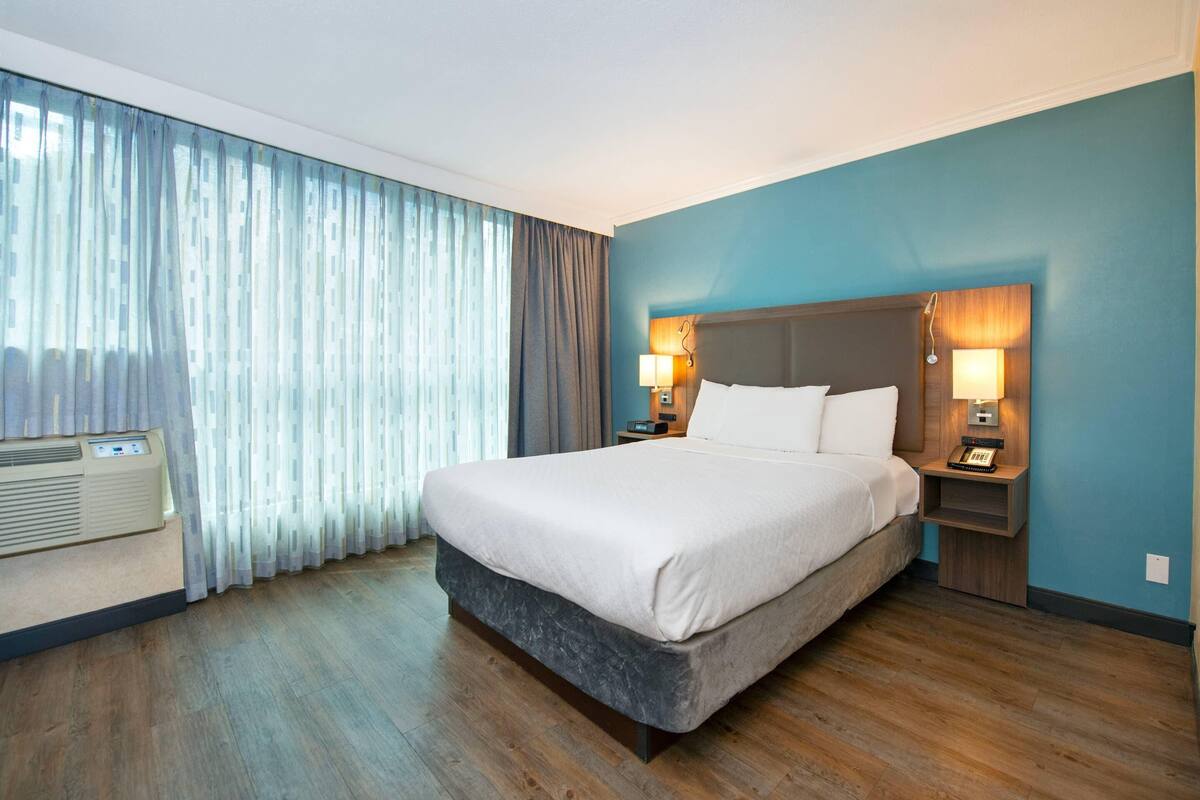 Une chambre d’hôtel avec un grand lit, deux tables de chevet avec des lampes, une fenêtre avec des rideaux et un climatiseur fixé au mur.