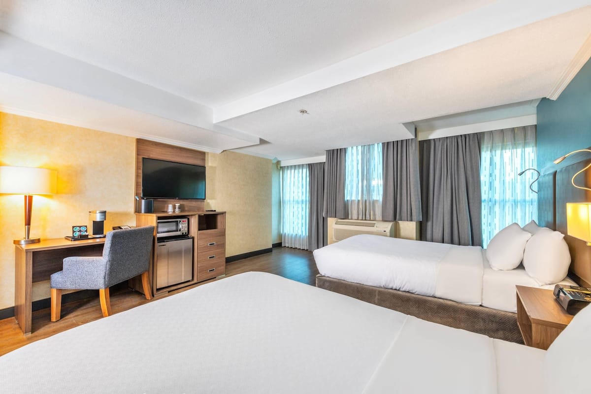 Une chambre d’hôtel comprenant un lit, un bureau avec une chaise, une télévision, un four à micro-ondes et une fenêtre avec des rideaux.