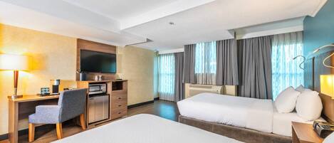 A hotel room with a bed, a desk with a chair, a television, a microwave, and a window with curtains.